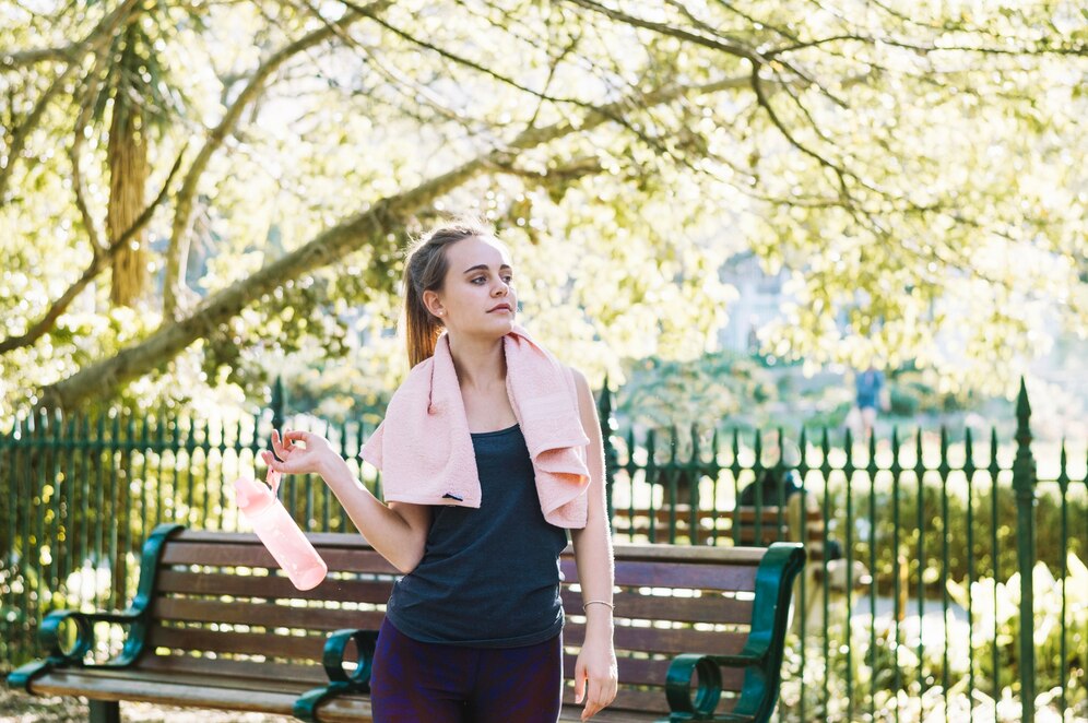 woman stands on a bench holding a towel, smiling as she enjoys the outdoors