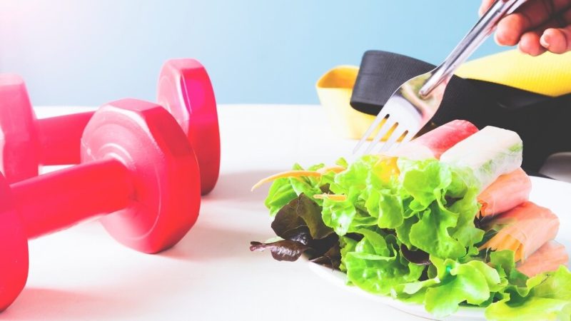 Healthy salad and gym dumbbells on a table, promoting a balanced lifestyle and fitness routine