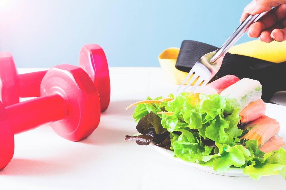 Healthy salad and gym dumbbells on a table, promoting a balanced lifestyle and fitness routine