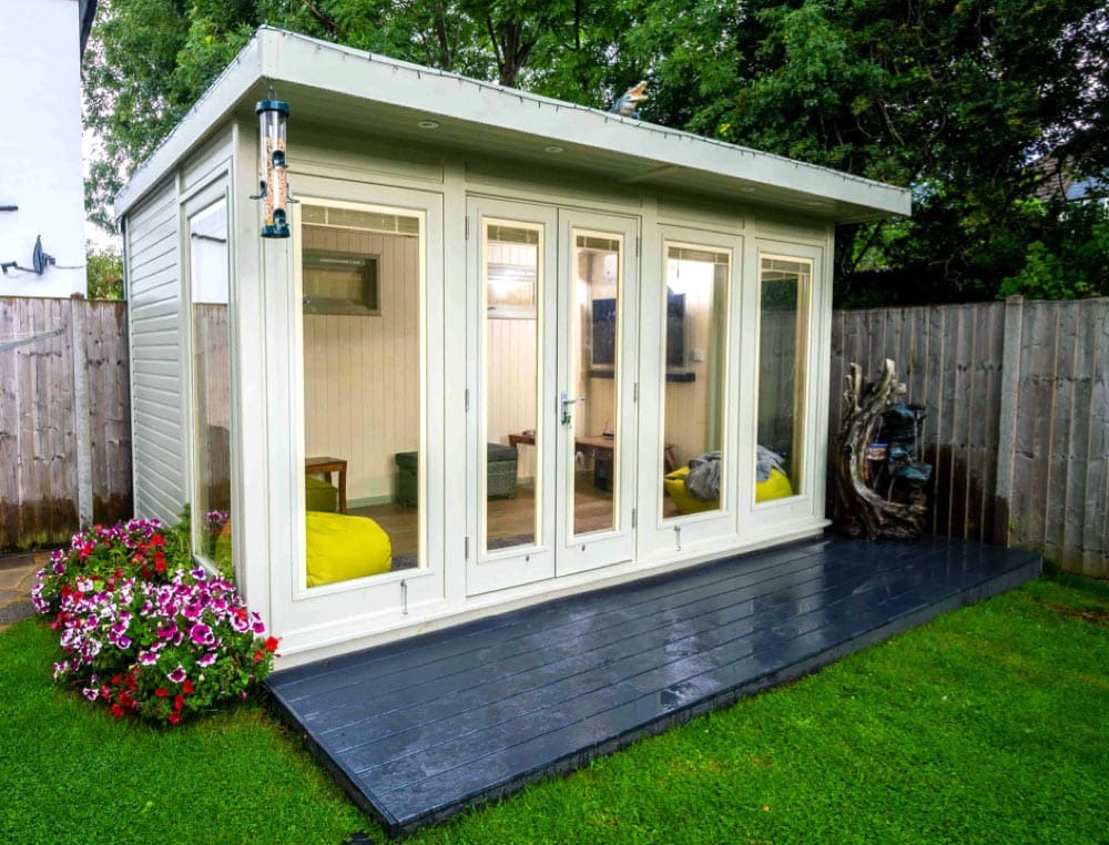 A garden office featuring a wooden deck and a white door, surrounded by greenery