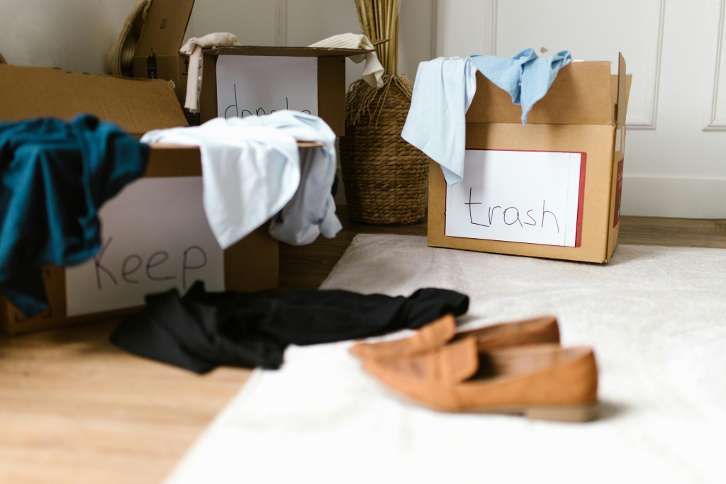 A cluttered room with cardboard boxes labelled "Keep," "Don't," and "Trash" filled with clothes