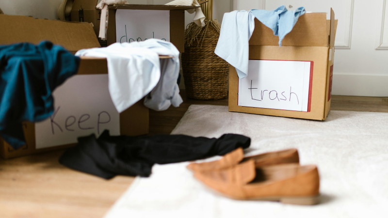 A cluttered room with cardboard boxes labelled "Keep," "Don't," and "Trash" filled with clothes